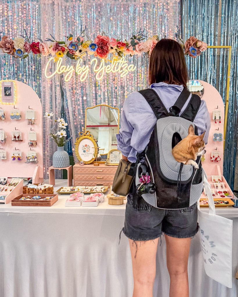 clay by Yelitza booth at Market for Makers 2025 in Houston for Leonie in Texas magazine by Minuit Studios - Colorful and glittery both with a neon sign including a trendy visitor and their cute dog in a backpack